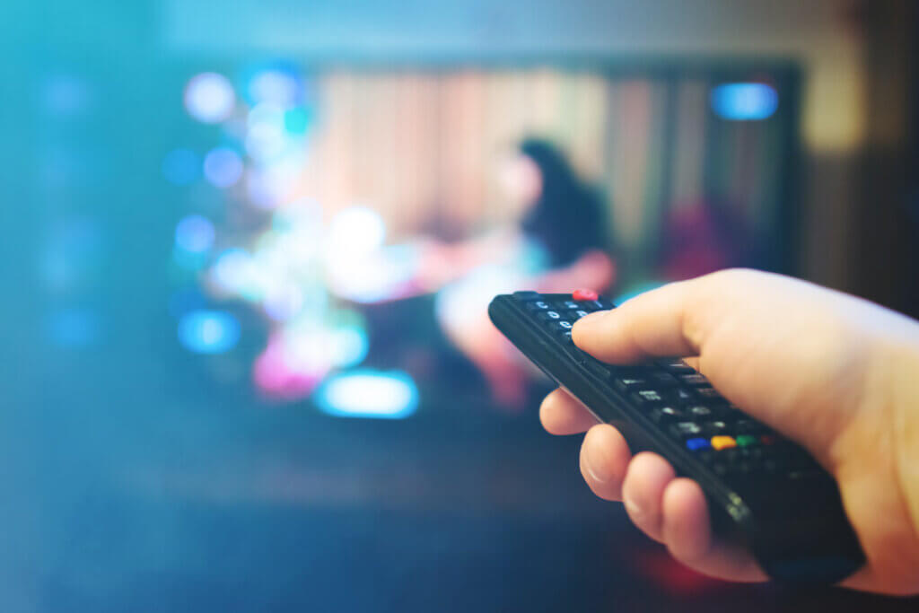 Person zeigt mit Fernbedienung auf Fernseher