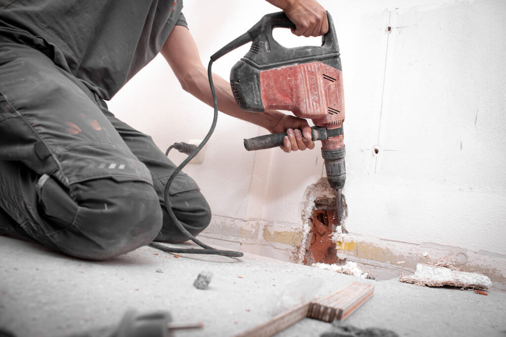 Installateur stemmt Loch mit Bohrhammer in die Wand.