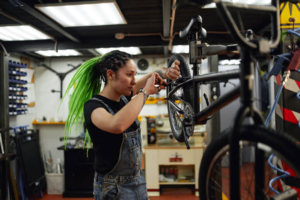 Mechanikerin schraubt am Hinterrad eines BMX-Bikes an einem Montageständer