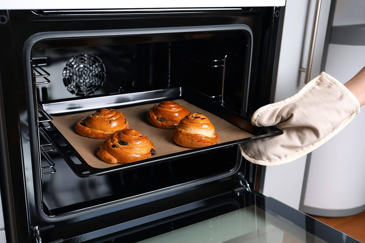 Person holt Rosinenschnecken aus dem Ofen