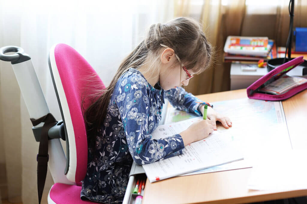 kind sitzt auf einstellbarem bürostuhl und macht hausaufgaben