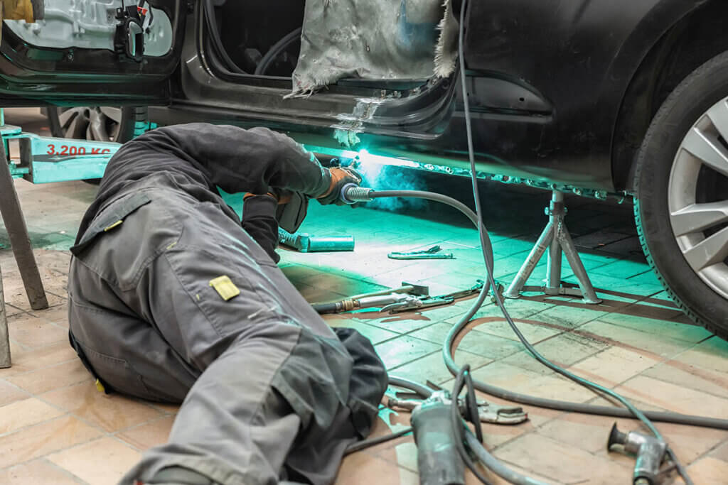 Person in Werkstatt schweisst am Auto